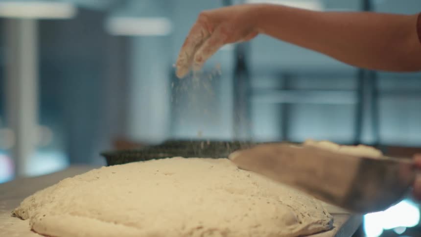 A person sprinkling flour on dough that is on a countertop