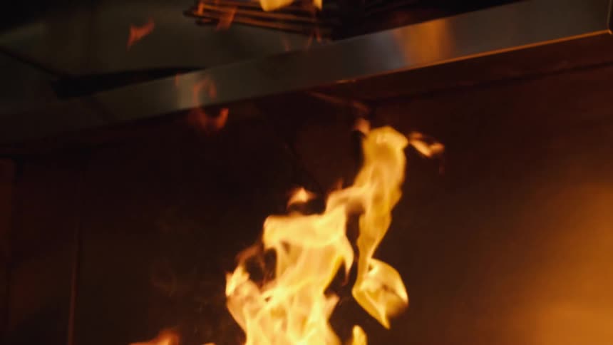 A cook pours oil in the pan causing a flame