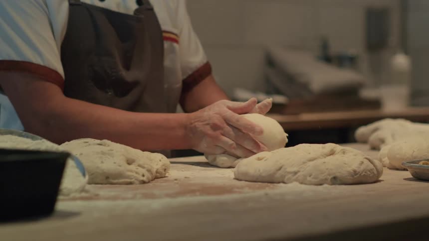 Woman working in restuarant kitchen shapes dough