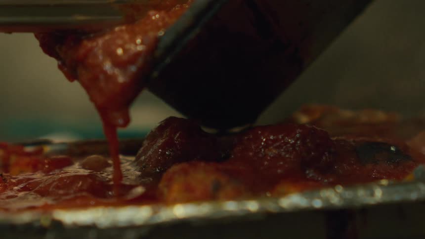 A person pouring hot salsa over a pan filled with meatballs