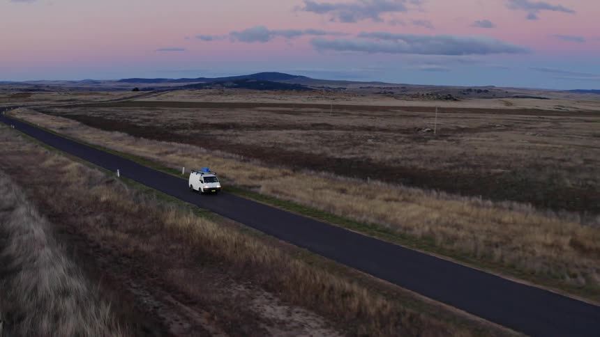 White van drives on a road through the countryside at sunset