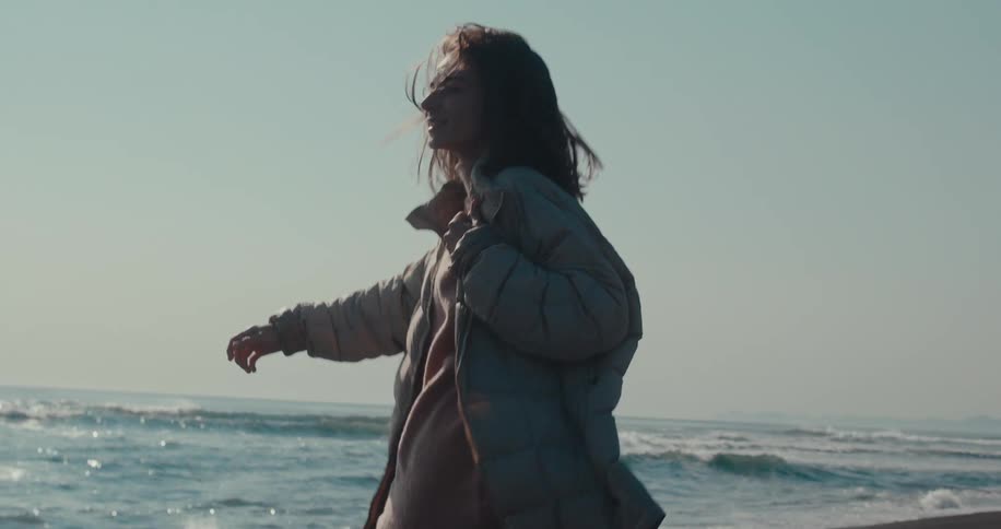 Happy woman wearing a coat prancing on the beach