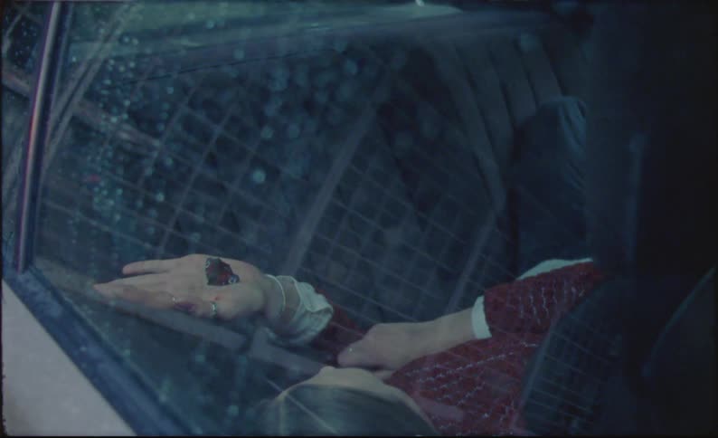 A woman is lying in the back seat of a car and there is a butterfly in her hand
