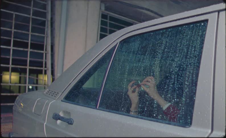 A person sits in the backseat of the car as it rains