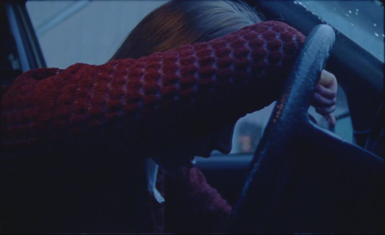 A woman is leaning against her steering wheel