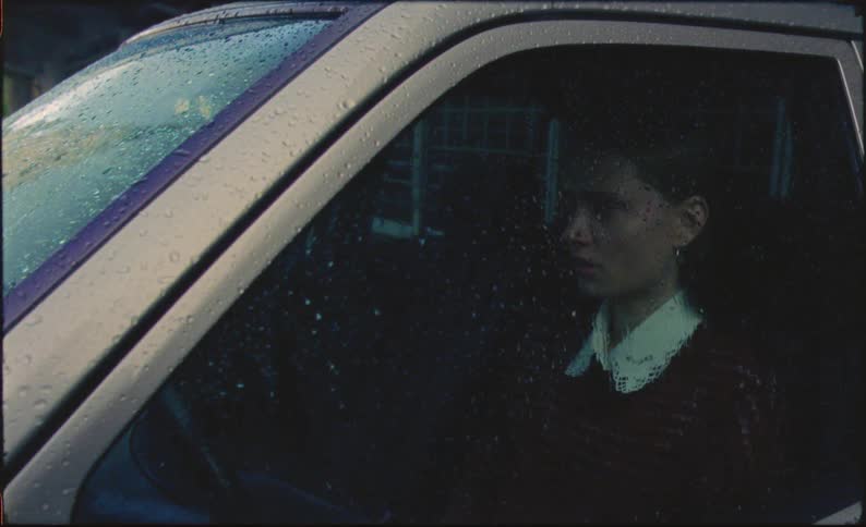 Woman sits in car on rainy day and leans her head against the steering wheel while she cries