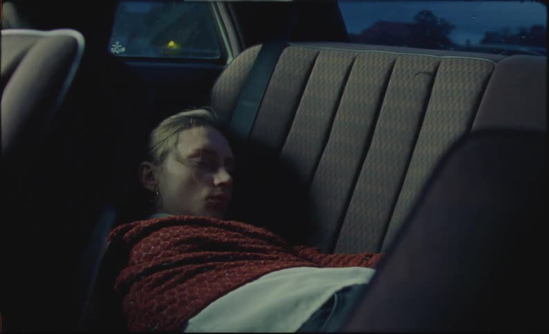 A woman is sleeping in the backseat of a car and then wakes up and gets up
