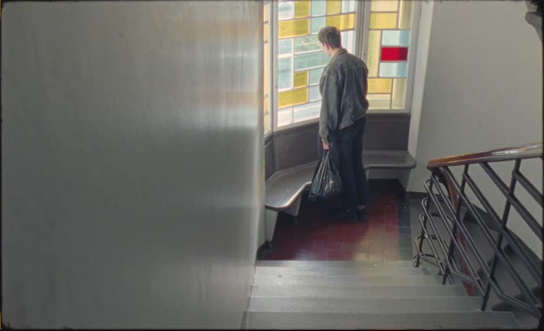 Man climbing stairs stops on landing to look out stained glass window
