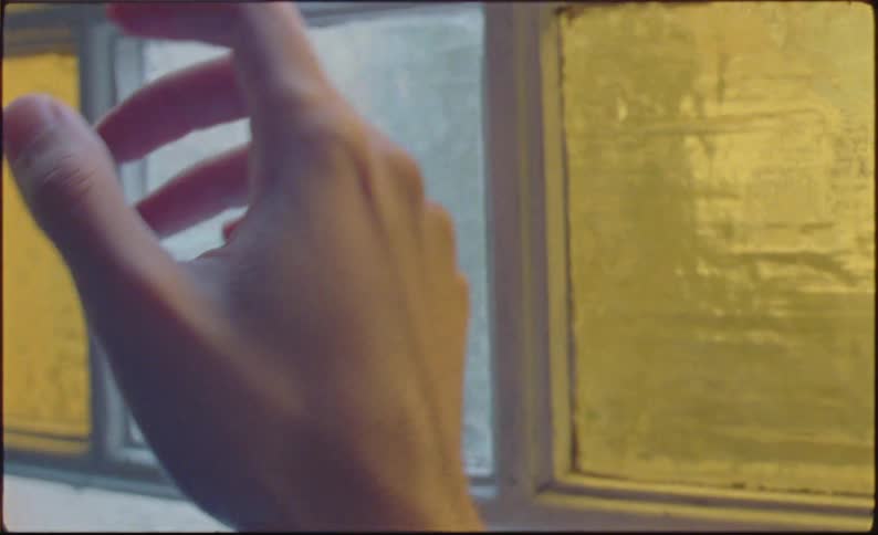 A hand reaching for a window with textured glass panes
