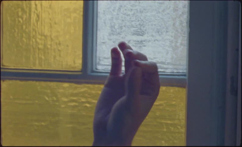 A hand reaching for a window with textured glass panes