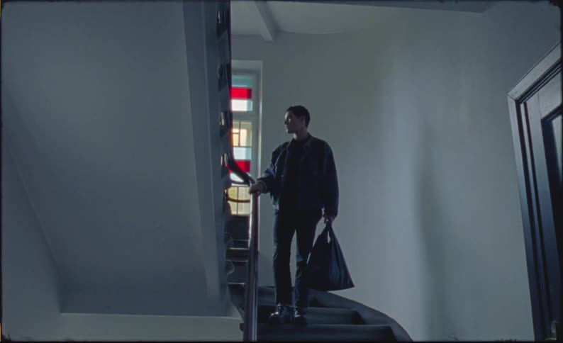 Man carrying a bag stands on a staircase next to a window with colored glass
