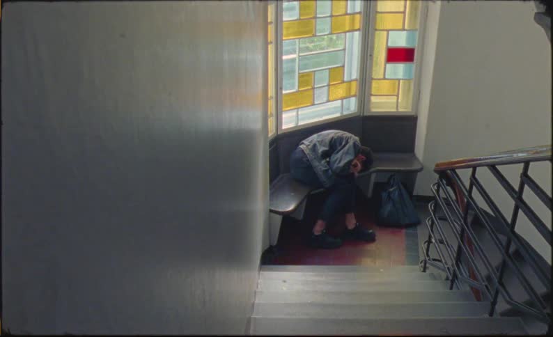 A man is sitting on a bench somewhere and lies down with a sad face and starts to cry