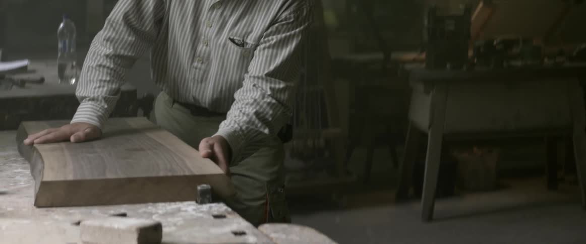 A wood worker inspects a piece of wood in a workshop