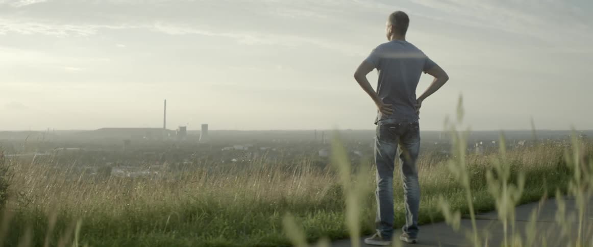A man is standing on a sidewalk overlooking a field
