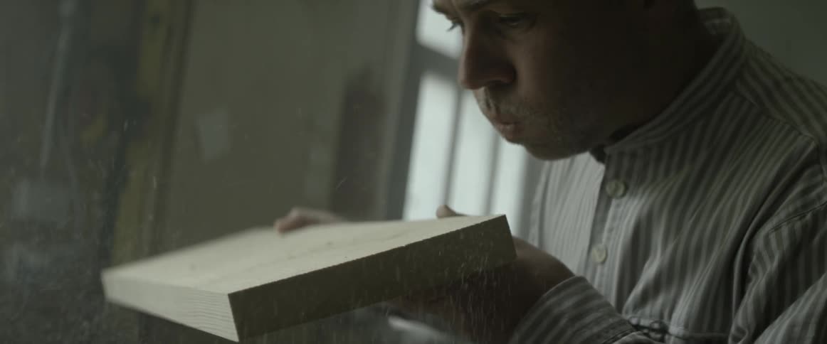 A man blows sawdust from a board