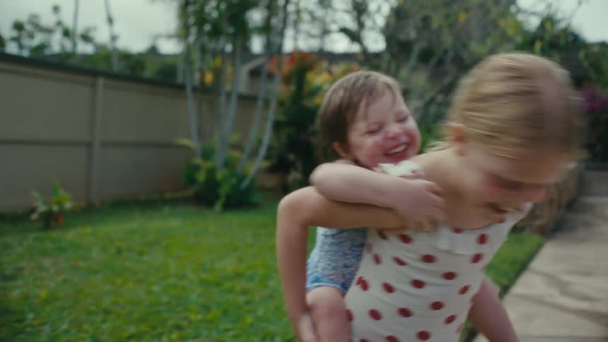 Older sister gives younger sister a piggyback ride and spins with her in backyard near swimming pool