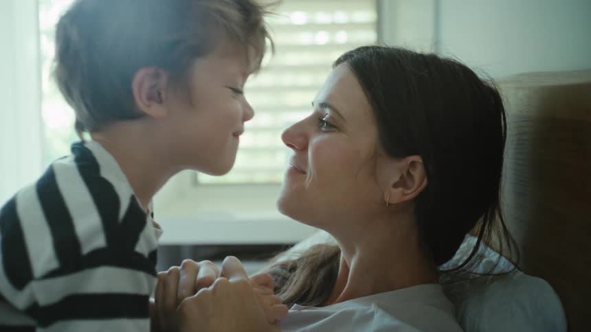 Mother lying on bed rubs noses with her son