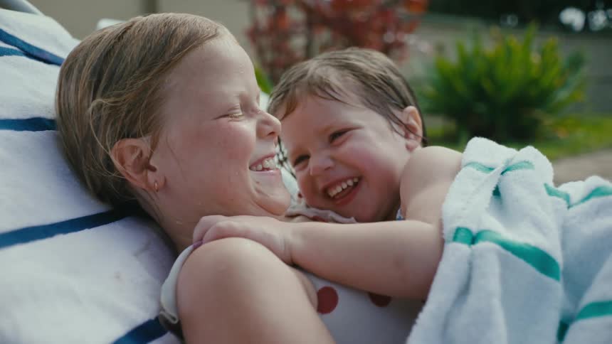 Sisters wet from water lie on chair in backyard and smile