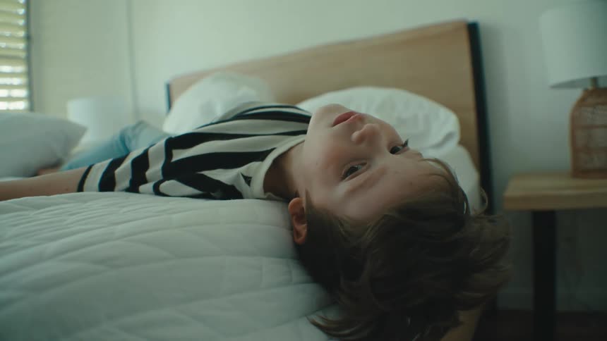 Boy lies on his back hanging his head off the bed