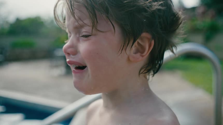 Close up of the face of a boy crying next to the swimming pool