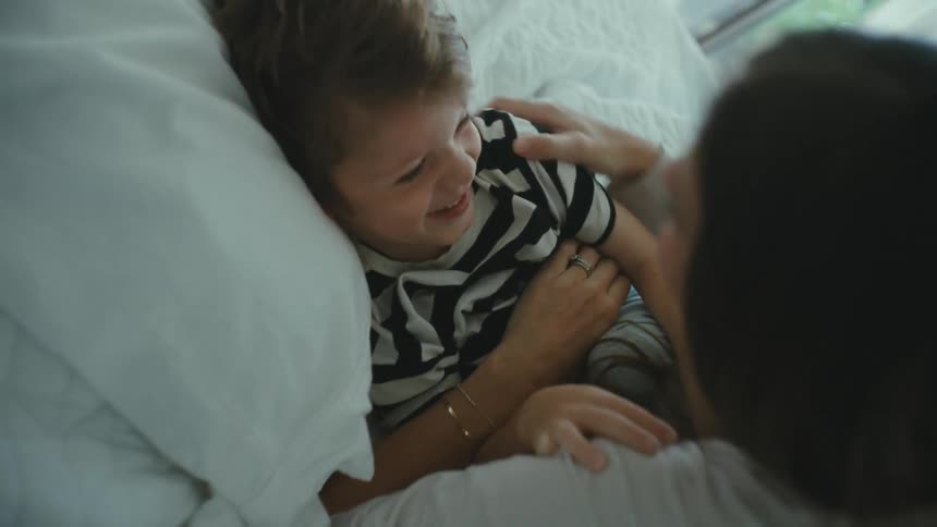 Mother and son playfully kissing and tickling in the bedroom