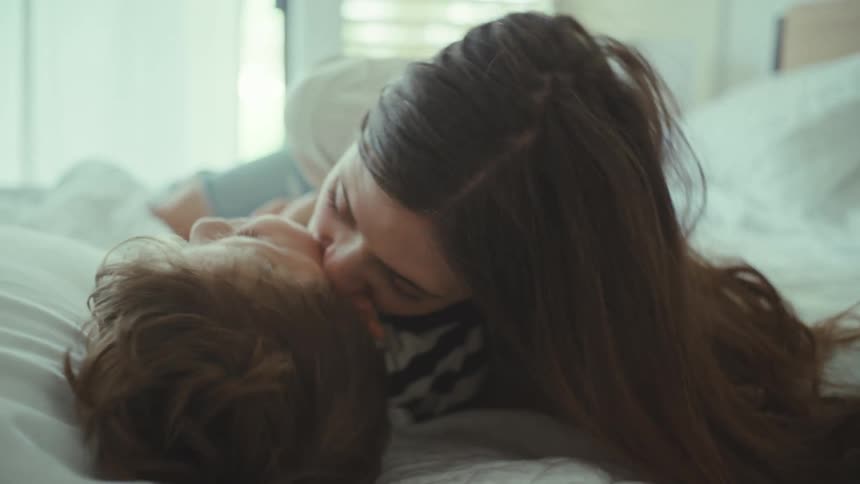 Mother and son playfully kissing and tickling in the bedroom