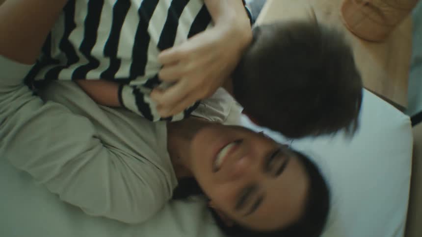Mother smiles while playing with son on bed