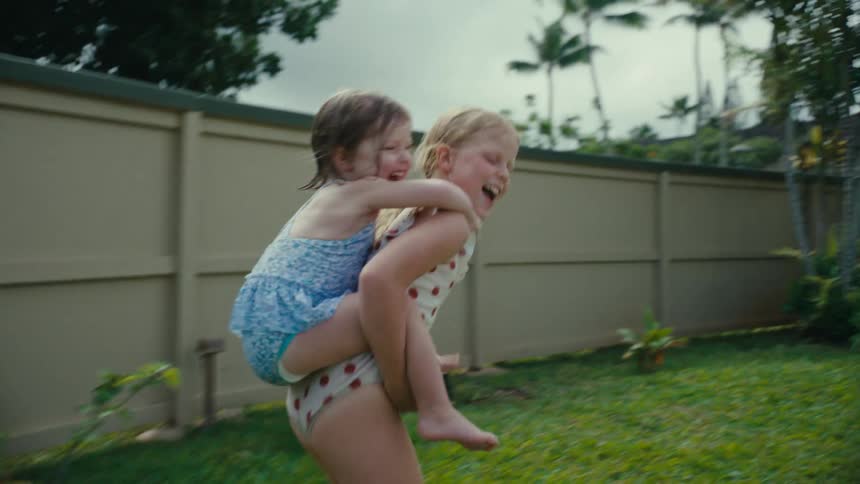 Two girls wearing swimsuits play in a backyard