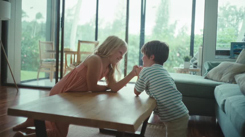 A boy and girl arm wrestling at a coffee table