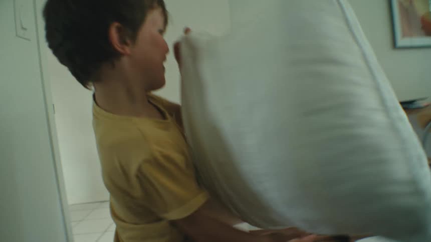 Mother and sons have a pillow fight at home in the bedroom