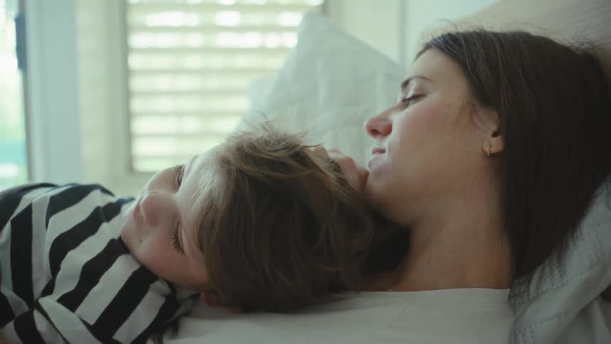 Mother and son embrace lying on bed indoors