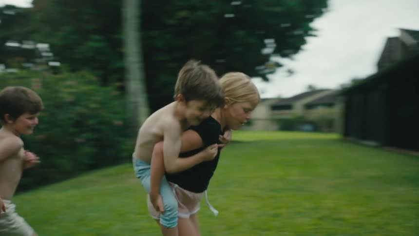Girl piggybacks younger boy as she and a third boy run in circles in the backyard
