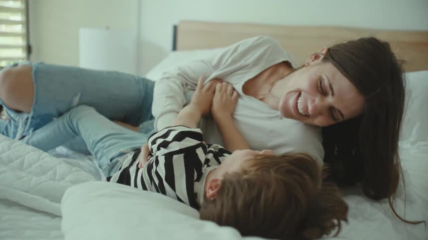 Mother and son playfully kissing and tickling in the bedroom
