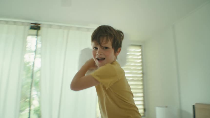 Boy over a bed pillow fights with the camera