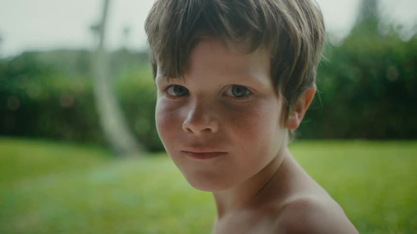 Face of a young shirtless boy in the backyard