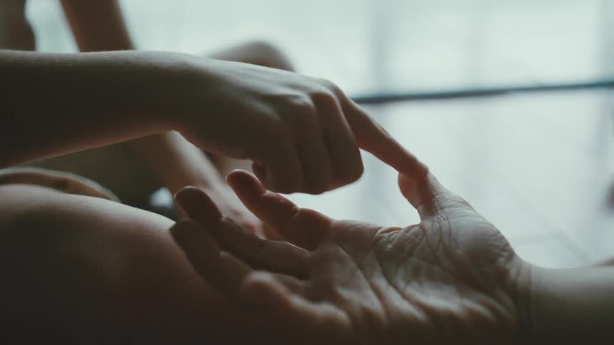 Child sitting down playing with another persons hands and fingers during day time