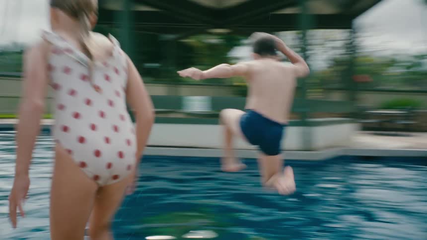 Siblings racing each other jump on the pool