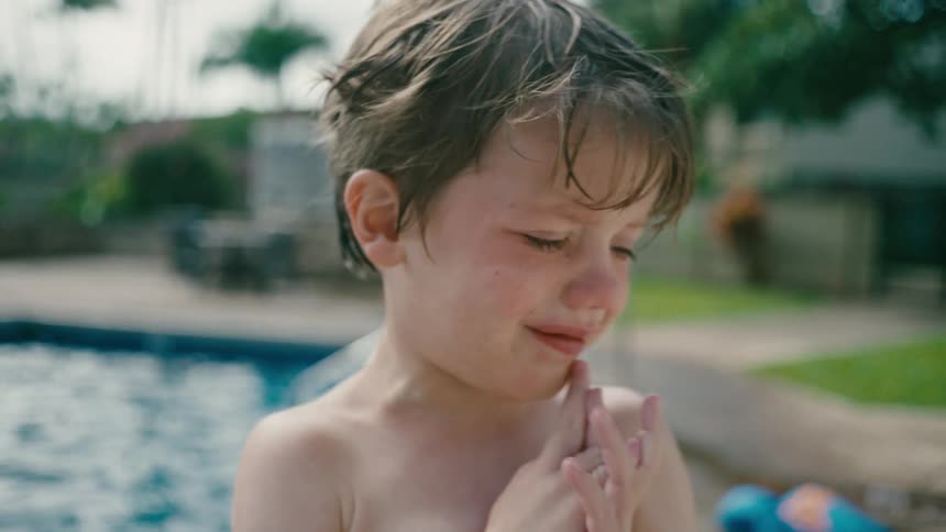 Boy stands outdoors near pool looking distressed