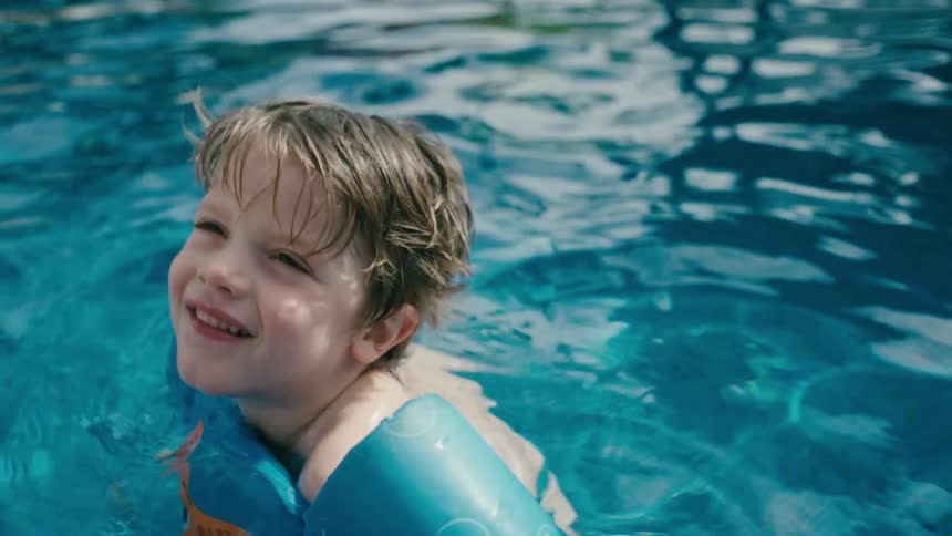 Boy with swim float sits in swimming pool