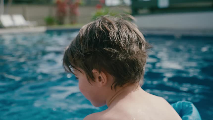 Boy sits on edge of swimming pool during the day