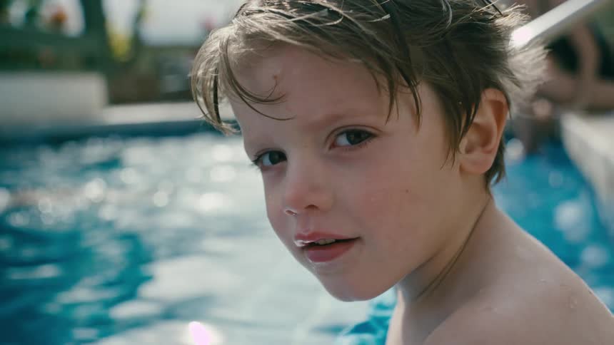 Close up of the face of a boy sitting at the side of a swimming pool