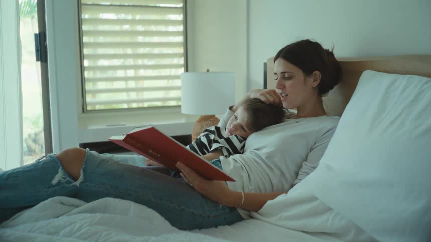 A mother reading a book to her son while laying around