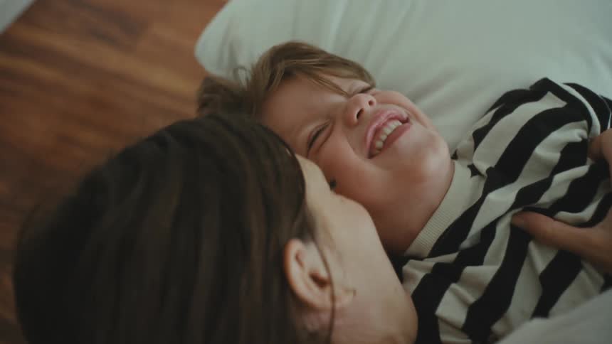 Mother and son playfully tickling each other in the bedroom