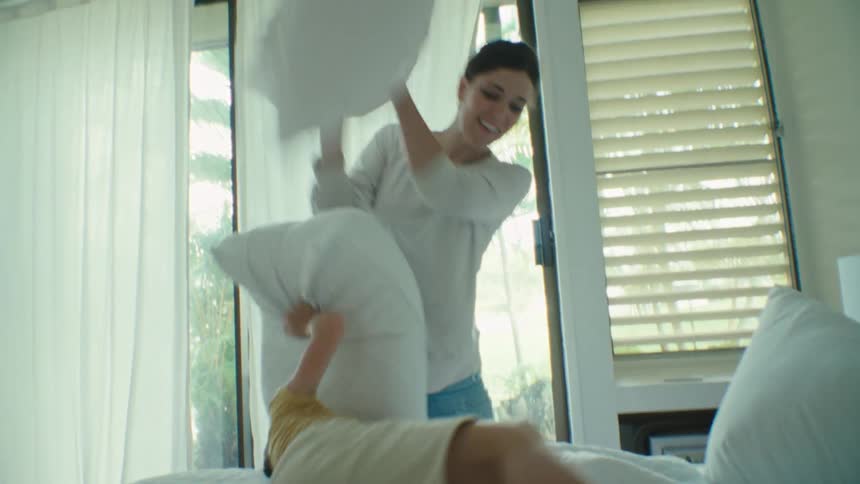 A young mother is having a pillow fight with her two sons in the bedroom