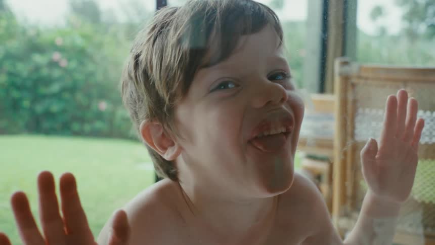 Boy in the backyard makes funny faces against the window