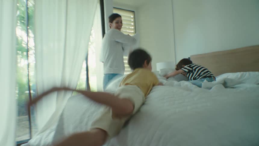 Mother and her two sons doing pillow fights inside the bedroom at midday