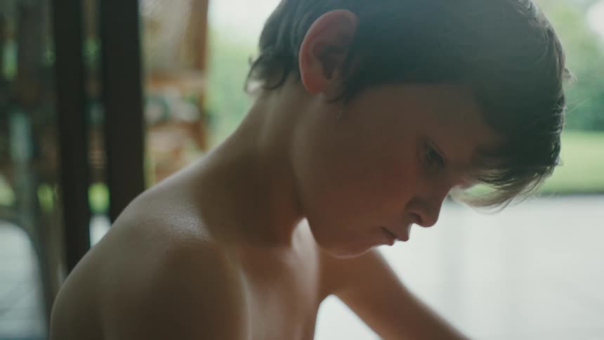Close up of the face of a shirtless boy sitting in the living room at home