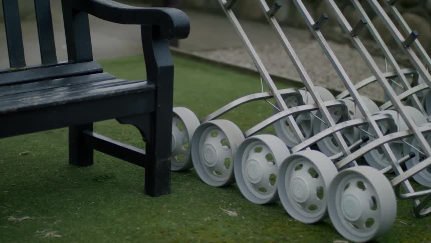 Multiple wheeled carts sit on turf between sidewalk and bench