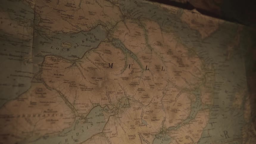 An old map hanging on the wall while the candlelight flickers
