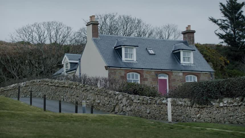 A stone house with a pink door and a bluegrey roof in a serene environment